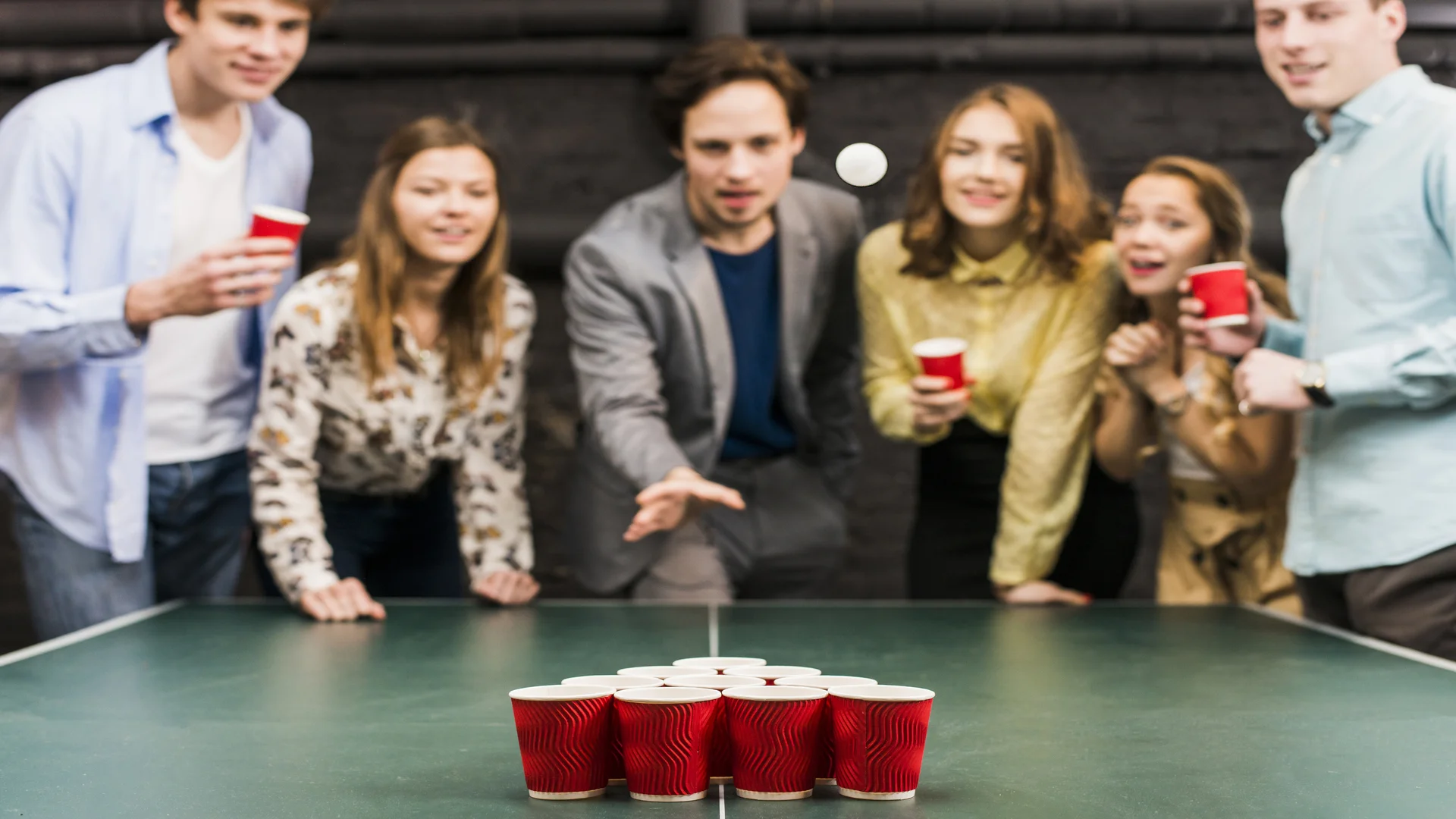 friends-looking-ball-while-man-playing-beer-pong-bar